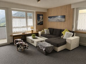 A modern living room with a sectional sofa, a coffee table, and a small side table. There are two cow-patterned ottomans and a potted plant on the side table. - Residenz Siesta Leukerbad # 4-bed apartment, Bad, WC by Interhome (Leukerbad)