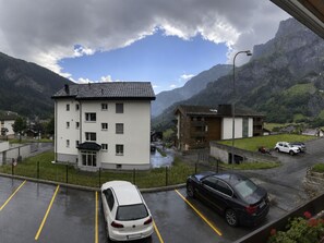A multi-story building with a flat roof, surrounded by a parking area with cars, and a mountainous landscape in the background. - Residenz Siesta Leukerbad # 4-bed apartment, Bad, WC by Interhome (Leukerbad)