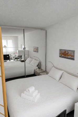 Ein Hotelzimmer mit einem großen Bett, einem Nachttisch, einem Schreibtisch mit Stuhl, einer Lampe und einem Bild an der Wand.