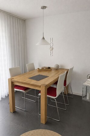 Ein Essbereich mit Holztisch, weißen Stühlen, einer Pendelleuchte und einer Wanddekoration.