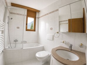 A bathroom with a bathtub, toilet, sink, and a window with a view of a mountain. - Residenz Darianne Leukerbad # 2-bed apartment, Bad, WC by Interhome (Leukerbad)
