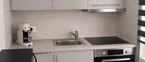 A modern kitchen with white cabinets, a coffee maker, a sink, a stove, and an oven.