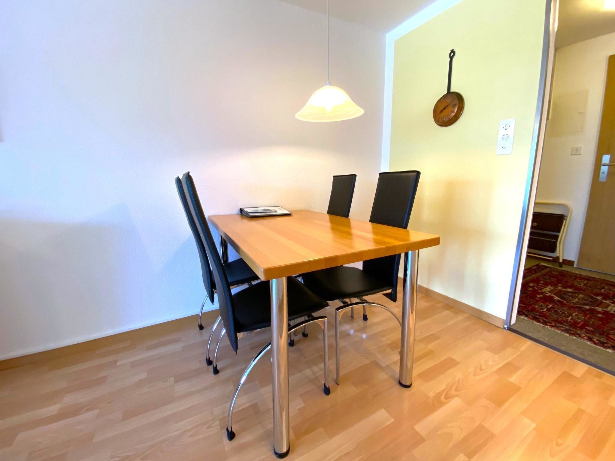 A dining area with a wooden table, four black chairs, and a hanging lamp.