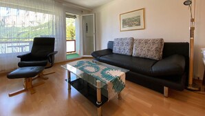 A living room with a black leather sofa, a black leather chair, a glass coffee table with a leaf-patterned runner, and a floor lamp. - Adler 82 # 2-bed apartment, Dusche, WC 2-Bettwohnung, Dusche, WC by Interhome (Leukerbad)