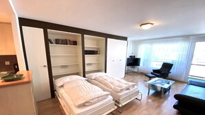 A bedroom with two beds, a bookshelf, a television, and a window. - Adler 82 # 2-bed apartment, Dusche, WC 2-Bettwohnung, Dusche, WC by Interhome (Leukerbad)