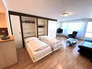 Ein Schlafzimmer mit zwei Betten, einem Bücherregal, einem Fernseher und einem Fenster.