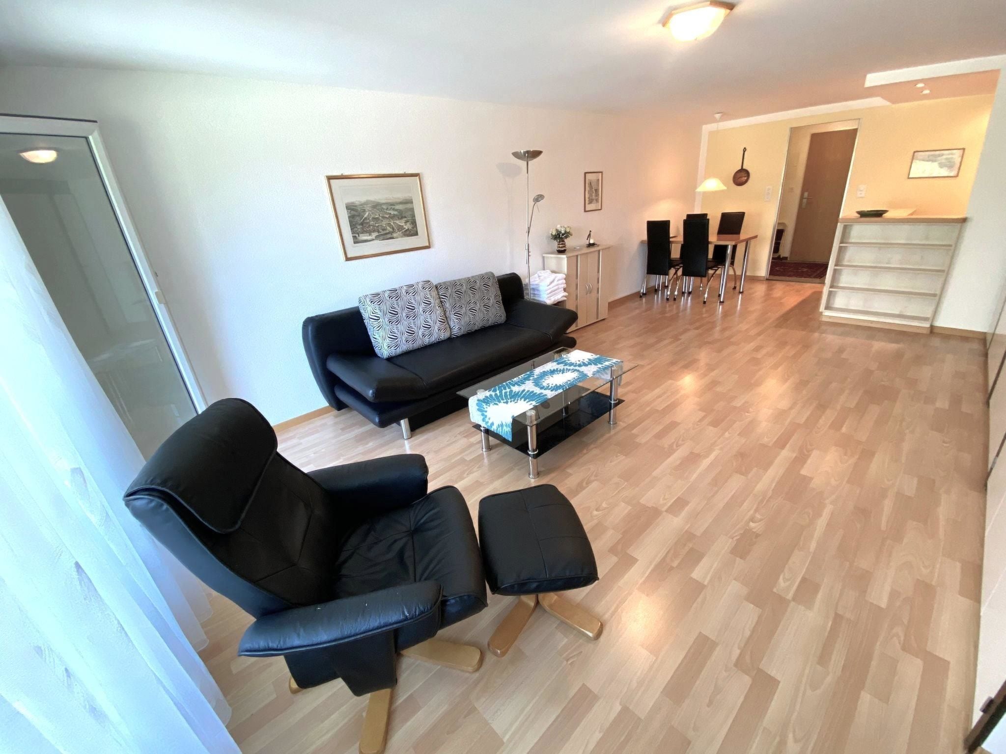 A modern living room with a black sofa, a glass coffee table, and a dining area with a white table and chairs.
