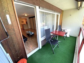 Ein Zimmer mit einer Schiebeglastür, die auf einen Balkon führt, einem kleinen Tisch, einem Stuhl und einer Couch.