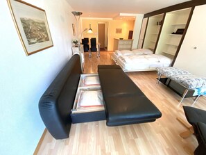 Um espaço compacto com sofá, cama, um banquinho e uma mesa com toalha de mesa estampada.