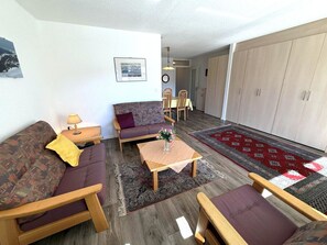 Een woonkamer met een bank, fauteuils, een salontafel en een eethoek met stoelen en een tafel.