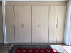 Een kamer met een grote kast, een kamerkleed met dessin, en een raam met gordijnen.
