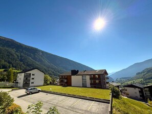 Ein Wohngebiet mit modernen Gebäuden, einem Parkplatz und einer Bergkulisse im Hintergrund.