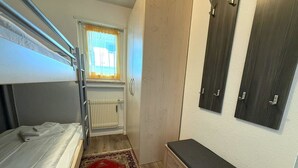 Een kleine kamer met een stapelbed, een bureau, een radiator en een raam met gordijnen.