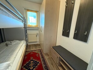 Ein kleines Zimmer mit einer Etagenbett, einem kleinen Schreibtisch, einer Heizung und einem Fenster mit Vorhängen.