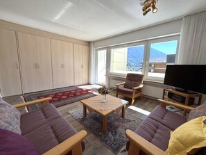 A modern living room with a sofa, armchairs, a coffee table, and a TV. There are large windows with a mountain view. - Salute 109 # 4-bed apartment, Dusche, WC 4-Bettwohnung, Dusche, WC by Interhome (Leukerbad)