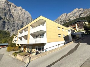 A multi-story building with balconies, a sign reading 'SALUTE', and a mountainous backdrop. - Salute 109 # 4-bed apartment, Dusche, WC 4-Bettwohnung, Dusche, WC by Interhome (Leukerbad)