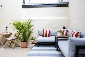 A cozy outdoor seating area with a sofa, cushions, a small table, a chair, and a potted plant. - 2BDR Brighton Retreat with Courtyard Garden (Brighton and Hove)