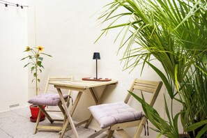 Een klein terras met een tafel, twee stoelen, een bloempot en een lamp.