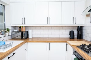 A kitchen with white cabinets, a wooden countertop, a coffee maker, and a microwave. - 2BDR Brighton Retreat with Courtyard Garden (Brighton and Hove)