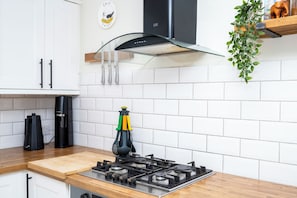 A kitchen with white tiled walls, a gas stove, a coffee maker, and a hanging plant. - 2BDR Brighton Retreat with Courtyard Garden (Brighton and Hove)