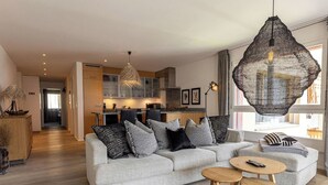 Ein modernes Wohnzimmer mit grauem Sofa, Couchtisch aus Holz und einer ungewöhnlichen gewebten Leuchte.