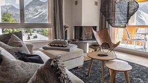 Ein modernes Wohnzimmer mit einer Couch, Sesseln, einem Kamin und Bergblick.
