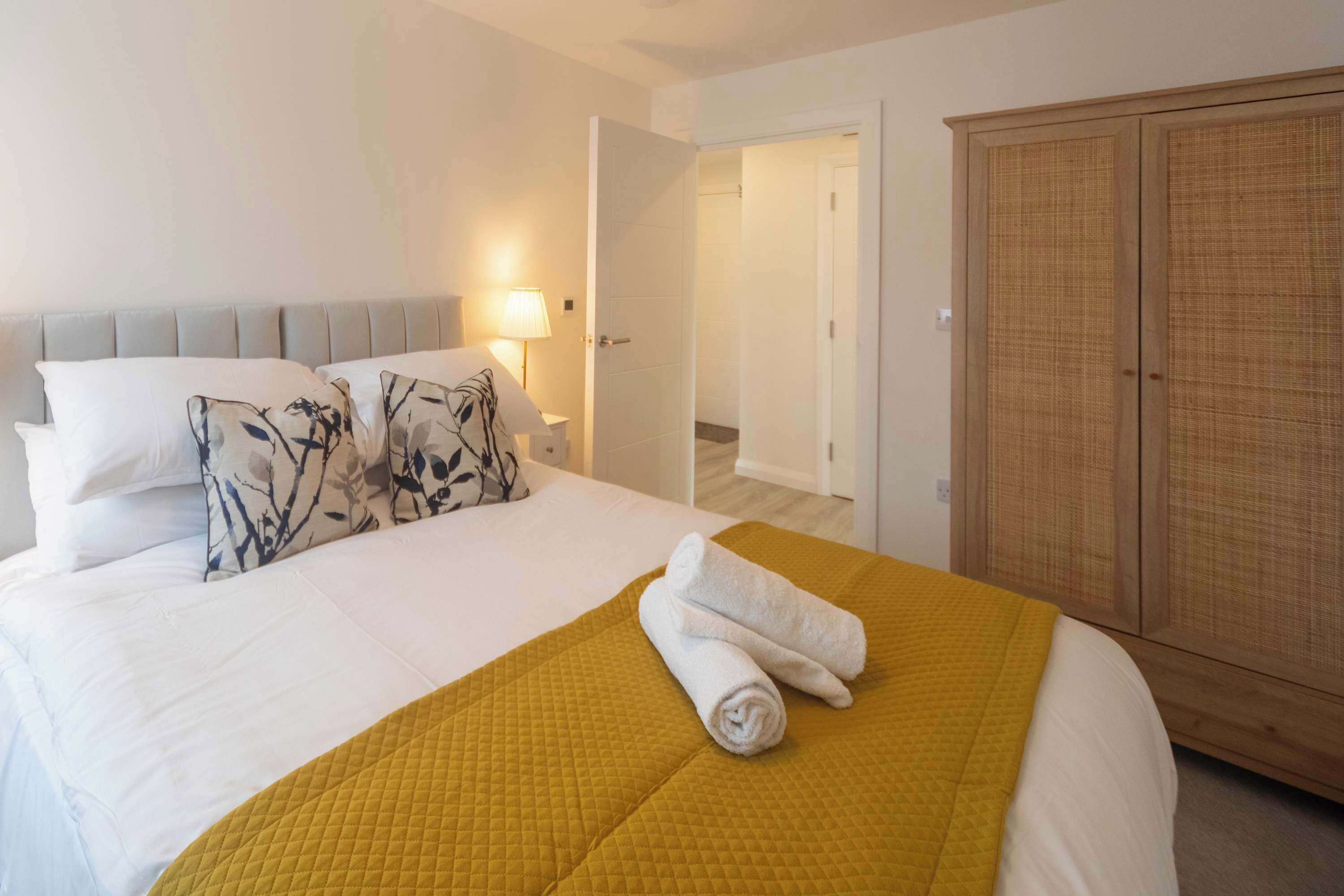 Quarto de hotel com cama, mesa de cabeceira, abajur e guarda-roupa.