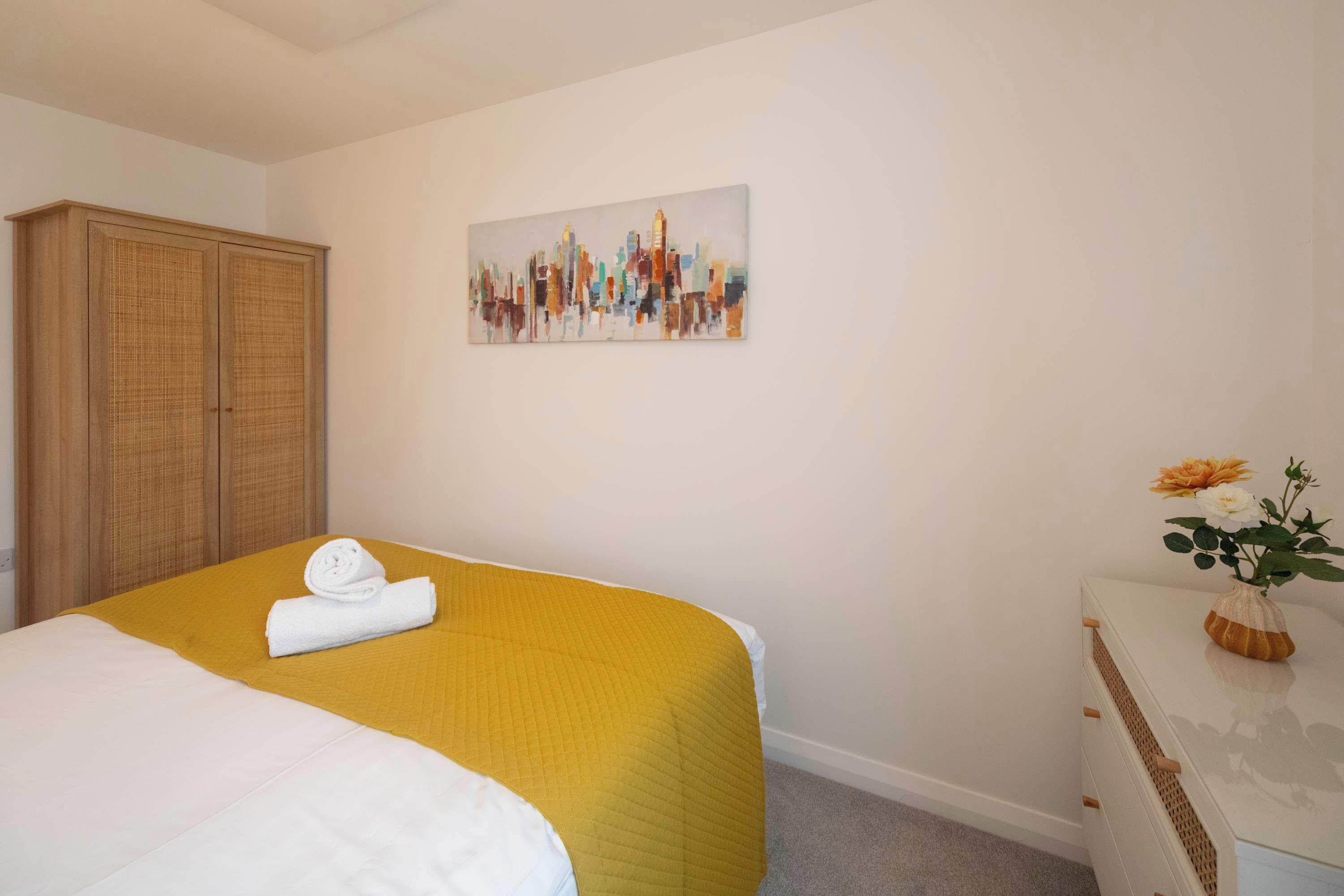 Ein Hotelzimmer mit einem Bett, einem Kleiderschrank, einem Gemälde und einem Schminktisch mit einer Vase.