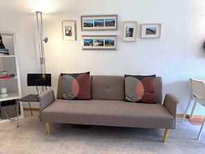 A neutral-toned sofa with patterned cushions, a floor lamp, a small table with a lamp, and a wall with framed pictures. - Fortuna 220 # 2-bed apartment, Dusche, WC 2-Bettwohnung, Dusche, WC by Interhome (Leukerbad)