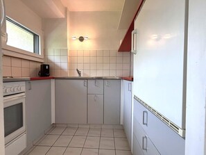 Ett kompakt kök med vita skåp, en inbyggd ugn, en kaffebryggare och ett fönster ovanför diskhon.