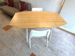 A dining table with a wooden top and white chairs in a room with a gray tiled floor and a gray wall. - Fortuna 220 # 2-bed apartment, Dusche, WC 2-Bettwohnung, Dusche, WC by Interhome (Leukerbad)