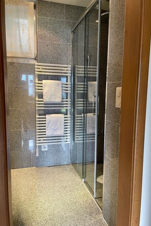 Un bagno moderno con cabina doccia in vetro, piastrelle in granito e portasci asciugamani integrato.