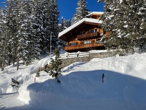 Un chalet in legno con un balcone, circondato da alberi innevati e un muro di pietra.