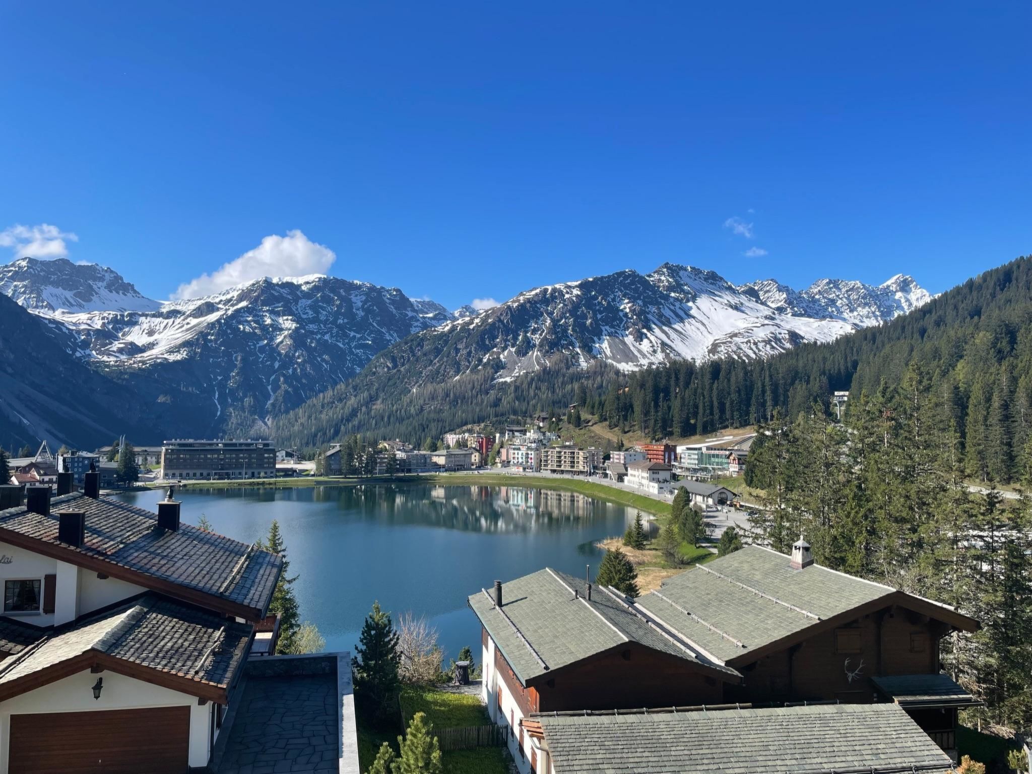 Eine Stadt am See mit Gebäuden und einem Berg im Hintergrund, bewölkter Himmel.