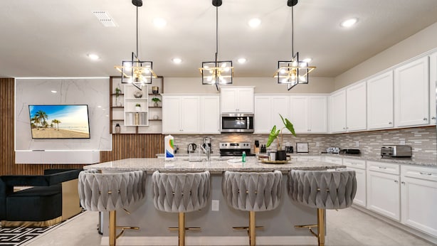 A modern kitchen with white cabinets, a central island with bar stools, a flat-screen TV, and pendant lighting. - 4305-Lana (Davenport)