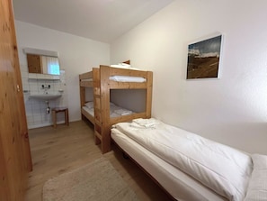 Een kleine, eenvoudige kamer met een stapelbed, een wastafel en een spiegel.