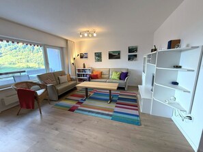 A modern living room with a sofa, a coffee table, a bookshelf, and a view of a mountainous landscape through the window. - Salve 8 # 5-bed apartment, Bad, WC 5-Bettwohnung, Bad, WC by Interhome (Leukerbad)