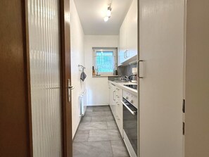A narrow kitchen with white cabinets, a window with a view, and a radiator on the floor. - Salve 8 # 5-bed apartment, Bad, WC 5-Bettwohnung, Bad, WC by Interhome (Leukerbad)