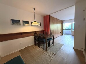 Ein Essbereich mit Tisch und Stühlen, einer Hängeleuchte und Blick durch eine Schiebetür auf einen Außenbalkon.