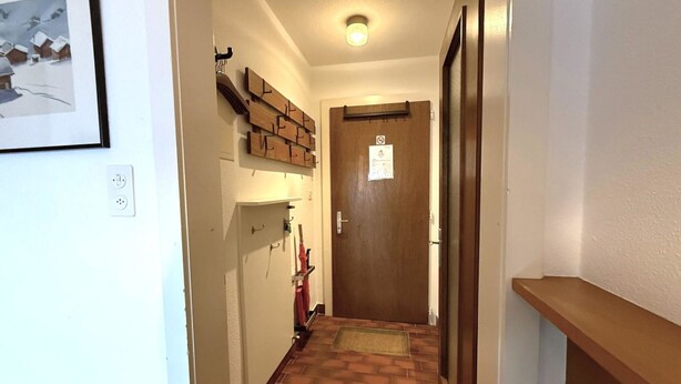 A narrow hallway with a wooden door at the end, a coat rack with items, and a framed picture on the wall. - Salve 8 # 5-bed apartment, Bad, WC 5-Bettwohnung, Bad, WC by Interhome (Leukerbad)