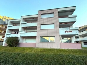 Un edifici de diversos pisos amb balcons, un rètol que diu 'Salve' i un paisatge de muntanya de fons.