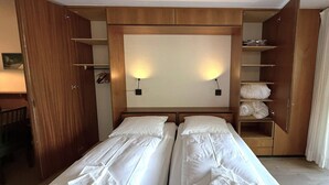 A hotel room with two beds, a wardrobe, a desk, and a shelf with towels. - Salve 8 # 5-bed apartment, Bad, WC 5-Bettwohnung, Bad, WC by Interhome (Leukerbad)