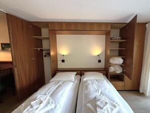 Ein Hotelzimmer mit zwei Betten, einem Schrank, einem Schreibtisch und einem Regal mit Handtüchern.
