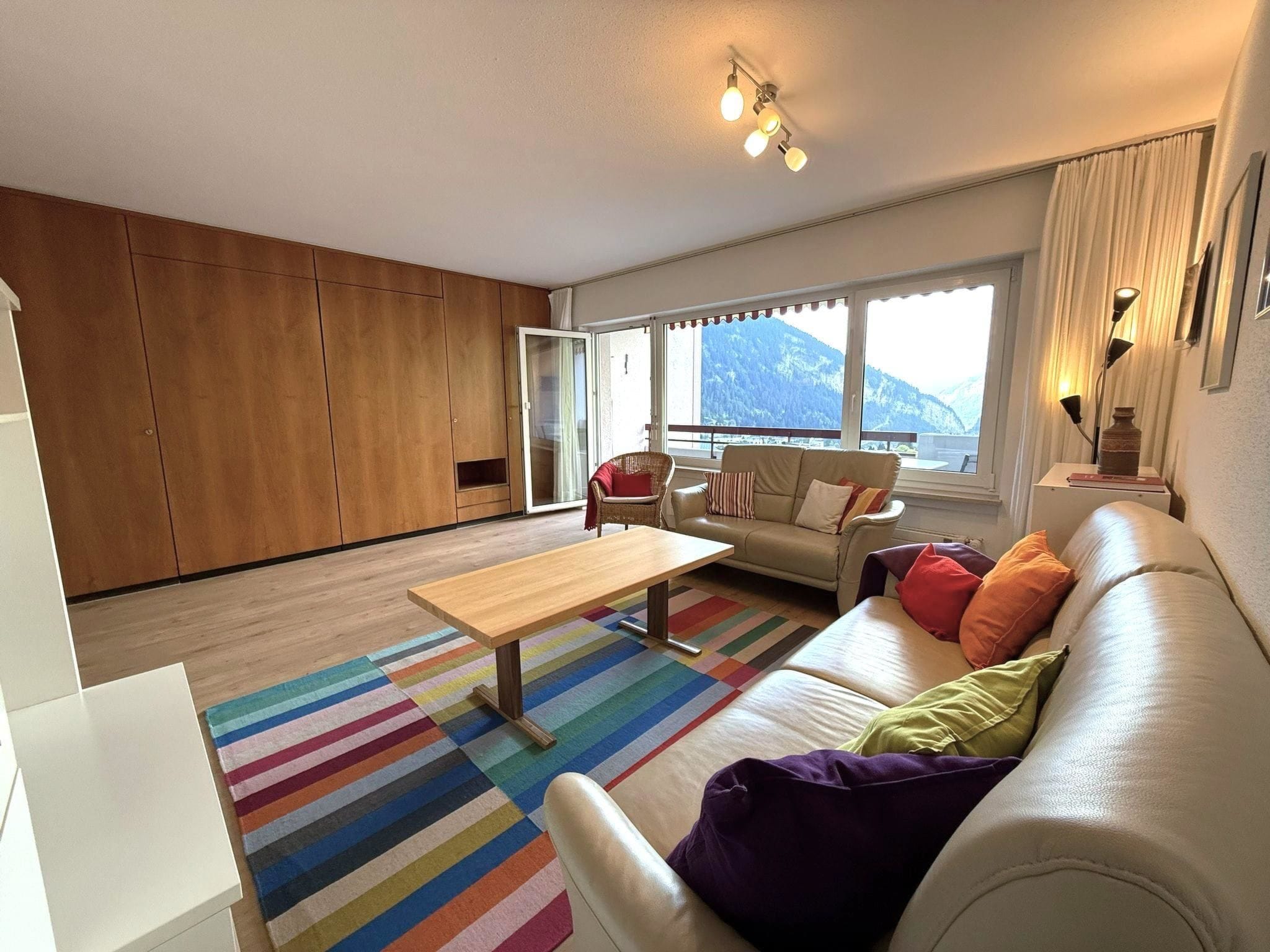 A modern living room with a sofa, a coffee table, and a view of mountains through large windows.