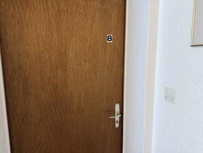 A wooden door with a number '8' sign, a door handle, and a white wall with a light switch. - Salve 8 # 5-bed apartment, Bad, WC 5-Bettwohnung, Bad, WC by Interhome (Leukerbad)