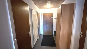 Käytävä, jossa on puiset ovet, musta matto sisäänkäynnin edessä ja kattovalaisin.