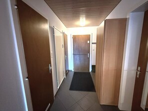 A hallway with wooden doors, a black mat at the entrance, and a ceiling light. - Salve 9 # 6-bed apartment, Dusche, WC 6-Bettwohnung, Dusche, WC by Interhome (Leukerbad)