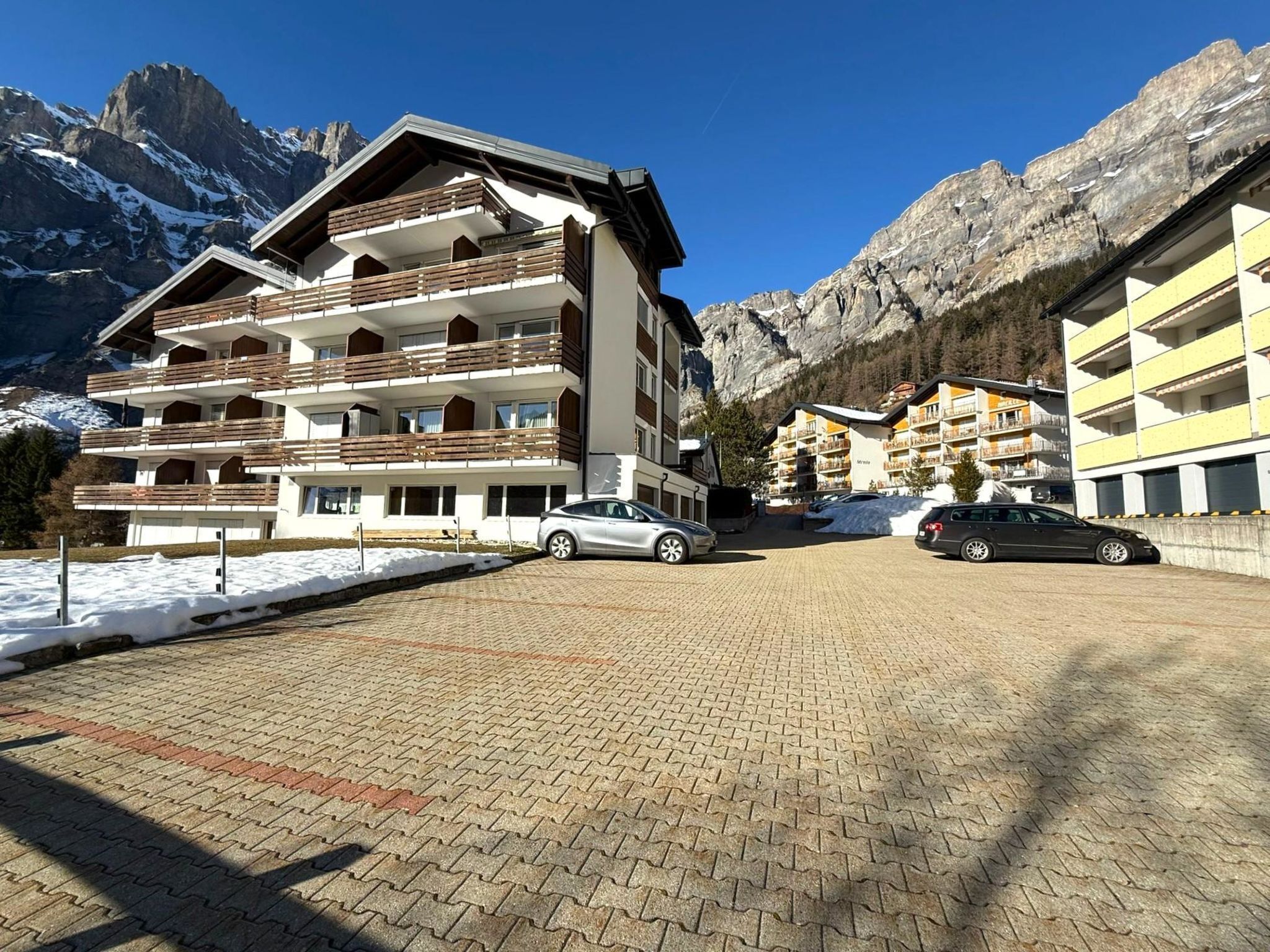 A multi-story hotel with balconies, a paved driveway, and a mountainous backdrop.