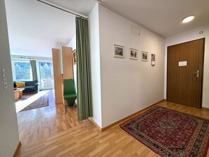 A hallway with a wooden floor, a green chair, a large rug, and a door with a sign. - Apollo 44 # 4-bed apartment, Bad, WC 4-Bettwohnung, Bad, WC by Interhome (Leukerbad)