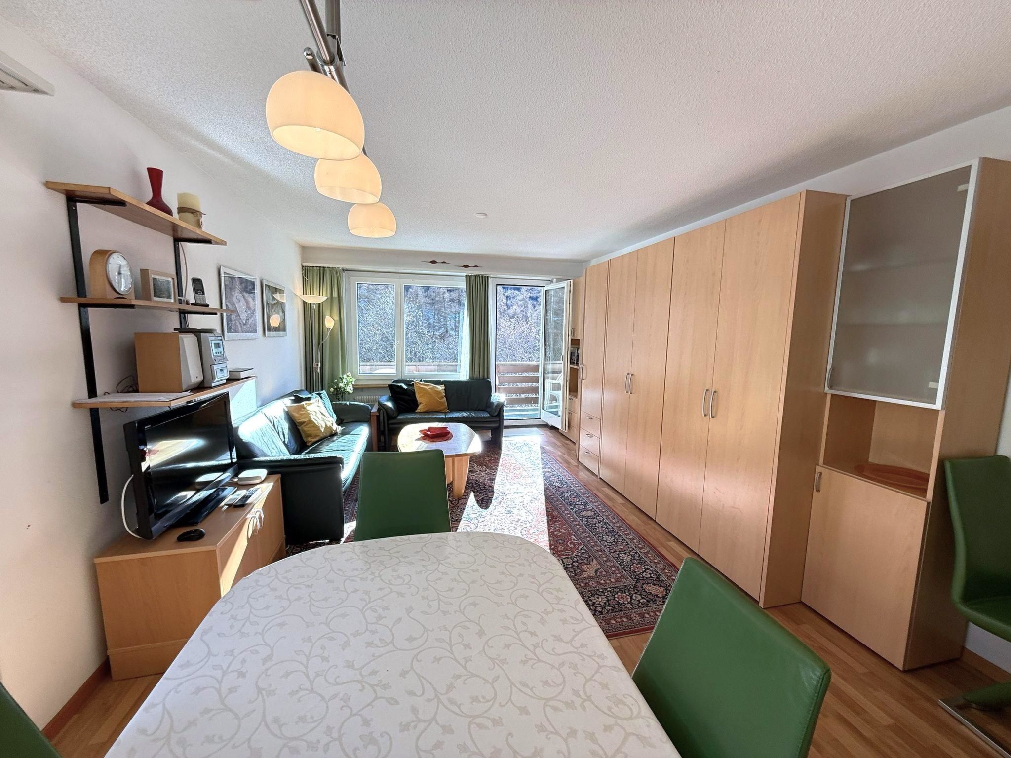 A modern living space with a dining area, a sofa, a coffee table, and a view of the outdoors through large windows.
